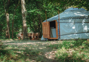 En traditionel jurte med udskårne trædøre i en skov, med bænk og bord, Camping Des Randonneurs, Frankrig.