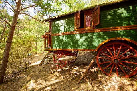 Caravana gitana sin baño privado en el bosque del Camping Des Randonneurs, Francia, con zona para sentarse fuera.