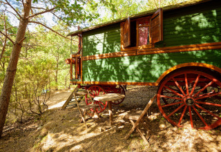 Caravana gitana sin baño privado en el bosque del Camping Des Randonneurs, Francia, con zona para sentarse fuera.