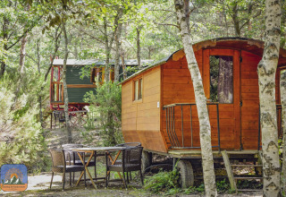 Zwei bunte Zigeunerwagen im Wald mit Gartentisch und Stühlen, ideal für naturnahes Camping.