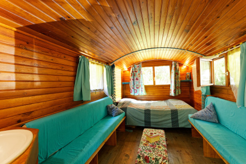 Interior de una acogedora cabaña Gipsy wagon de madera sin baño privado, con cama, sofás y cortinas coloridas.