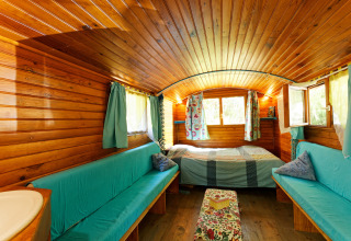 Interior de una acogedora cabaña Gipsy wagon de madera sin baño privado, con cama, sofás y cortinas coloridas.