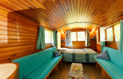 Gemütlicher Innenraum eines Gipsy Wagon aus Holz ohne eigenes Bad, mit Bett, Sofas und bunten Vorhängen.
