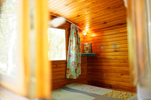 Binnenkant van de Gipsy wagon met houten wanden, een fleurig gordijn en raam, geen privébadkamer.