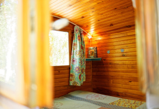 Binnenkant van de Gipsy wagon met houten wanden, een fleurig gordijn en raam, geen privébadkamer.