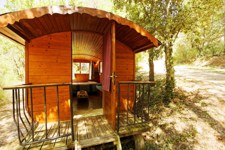 Cabaña carromato gitano de madera sin baño privado, puerta abierta y entorno boscoso iluminado.