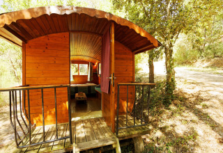 Cabaña carromato gitano de madera sin baño privado, puerta abierta y entorno boscoso iluminado.
