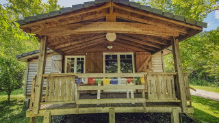 Træchalet med veranda på Camping des Randonneurs i Frankrig omgivet af grønne træer og solrigt vejr