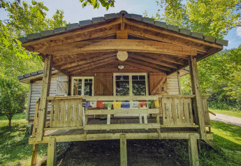 Træchalet med veranda på Camping des Randonneurs i Frankrig omgivet af grønne træer og solrigt vejr