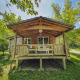 Træchalet med veranda på Camping des Randonneurs i Frankrig omgivet af grønne træer og solrigt vejr