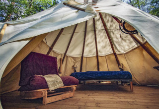 Binnenzicht van een Wigwam-tipi met houten vloer, bed en zetel bij Camping Des Randonneurs, Frankrijk.