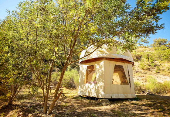 Tipi burbuja único sin plomería, rodeado de árboles verdes y colinas en un entorno natural soleado.