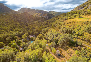 Vista aérea de montañas, bosque, camino y tiendas tipis en Camping Des Randonneurs, Francia.