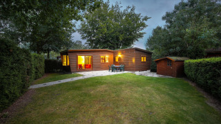 Aftenfoto af Cozy Chalet ved Bungalowpark Het Verscholen Dorp i Holland, omgivet af grønne træer.