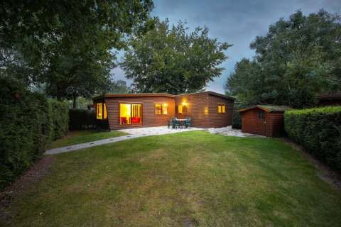 Evening view of Cozy Chalet at Bungalowpark Het Verscholen Dorp, Netherlands, surrounded by lush greenery.