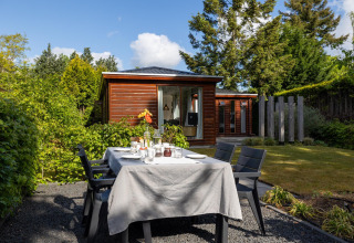 Gedeckter Gartentisch vor einem kleinen Holzhaus im Bungalowpark Het Verscholen Dorp, Niederlande.