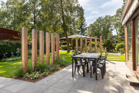 Buitenterras aan Cozy Chalet in Bungalowpark Het Verscholen Dorp met tafel, stoelen en houten palen.