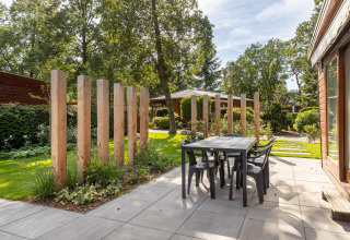 Outdoor patio at Cozy Chalet, Bungalowpark Het Verscholen Dorp, Netherlands, with modern table, chairs and wood poles.