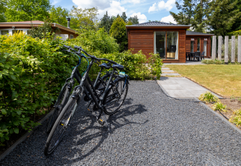 Tres bicicletas negras aparcadas en un sendero de grava frente a una pequeña casa de madera en Cozy Chalet, Het Verscholen Dorp.