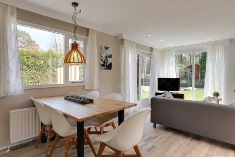 Lichte woonruimte in Cozy Chalet van Bungalowpark Het Verscholen Dorp met tafel, zetel en tuinzicht.