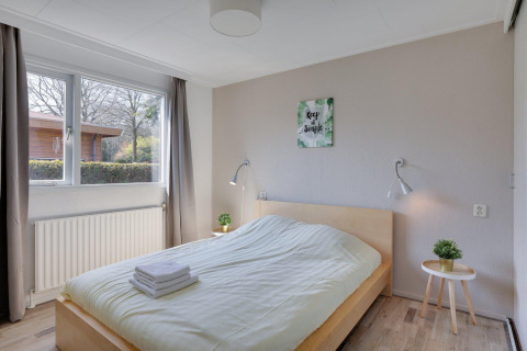 Lyst soveværelse i Cozy Chalet på Bungalowpark Het Verscholen Dorp med stort vindue og enkel indretning.