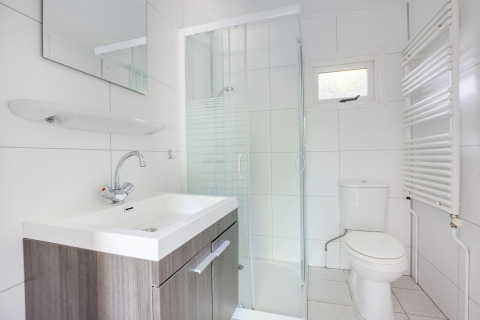 Salle de bain blanche moderne en tiny house avec douche, lavabo, miroir et WC aux Pays-Bas.