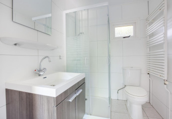 Modernes, weiß gefliestes Badezimmer im Tiny House mit Dusche, Waschbecken, Spiegel und WC.