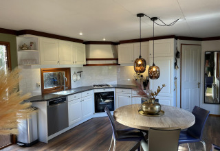 Moderne compacte keuken en eetplaats met ronde tafel, hanglampen en houten accenten in een Vlaamse tiny house.