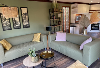 Acogedora sala de Chalet en los Países Bajos con sofás verdes, decoración moderna y cocina abierta al fondo.