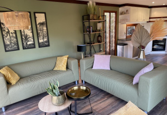 Acogedora sala de Chalet en los Países Bajos con sofás verdes, decoración moderna y cocina abierta al fondo.