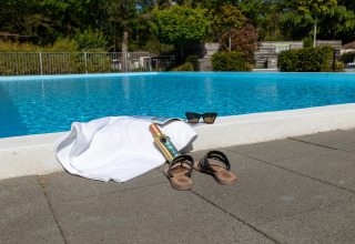 Escena de piscina en Cozy Chalet, Bungalowpark Het Verscholen Dorp, Países Bajos, con toalla y sandalias.