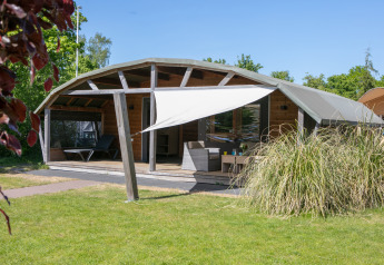 Udendørs lodge med terrasse og markise, beliggende i Holiday Park 't Rheezerwold i Holland, omgivet af grønne områder.