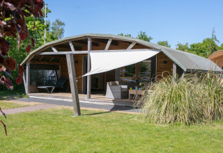 Outdoor lodge met overdekt terras bij Holiday Park 't Rheezerwold in Nederland, omgeven door natuur.