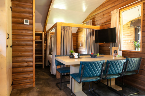 Gemütliche Innenaufnahme einer Outdoor Lodge mit Esstisch, blauen Stühlen und Holzwänden im Holiday Park 't Rheezerwold.