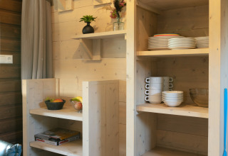 Estanterías de cocina en una lodge al aire libre con platos y fruteros en Holiday Park 't Rheezerwold, Países Bajos.