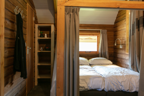 Dormitorio de cabaña con cama doble, estantería y ventana en Outdoor lodge del Holiday Park 't Rheezerwold, Países Bajos.