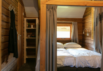 Dormitorio de cabaña con cama doble, estantería y ventana en Outdoor lodge del Holiday Park 't Rheezerwold, Países Bajos.