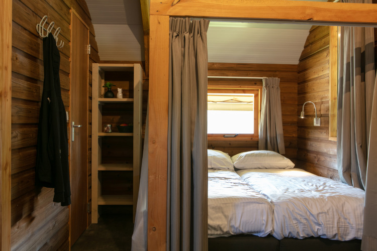 Innenraum einer Holzlodge mit Doppelbett, Regal und Fenster im Outdoor Lodge im Holiday Park 't Rheezerwold, Niederlande.
