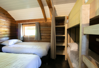 Photo intérieure d’une lodge Outdoor confortable, avec lits simples et lits superposés en bois dans un parc de vacances.