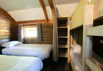 Foto degli interni di una confortevole Outdoor lodge con letti singoli e letti a castello in legno in un parco vacanze.