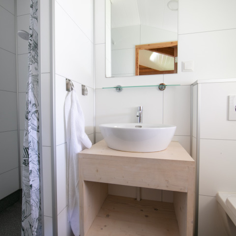 Moderne badkamer met spiegel, witte waskom en houten meubel in de Outdoor lodge bij 't Rheezerwold, Nederland.