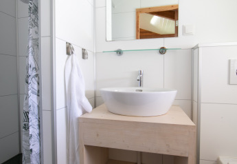 Bagno moderno con lavabo rotondo, specchio, ripiano in vetro e asciugamano presso Outdoor Lodge nei Paesi Bassi.