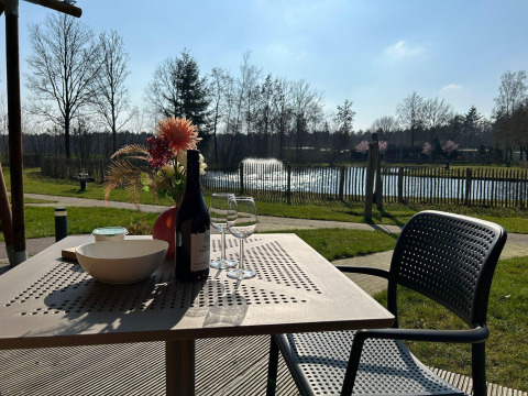 Zicht vanuit een luxe safaritent in Vakantiepark 't Rheezerwold, Nederland, met wijn en bloemen op tafel.