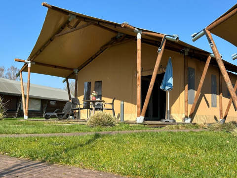 Luxe tentlodge in Holiday Park 't Rheezerwold in Nederland, met terras en buitenmeubilair zichtbaar.