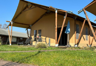 Luxe tentlodge op vakantiepark 't Rheezerwold in Nederland, met terras en buitenzitje zichtbaar.
