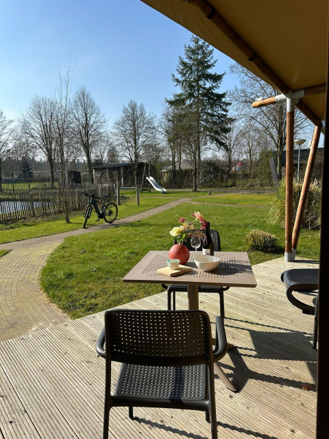 Vue depuis la terrasse d'une tente de luxe au Holiday Park 't Rheezerwold, Pays-Bas, avec jardin et aire de jeux.
