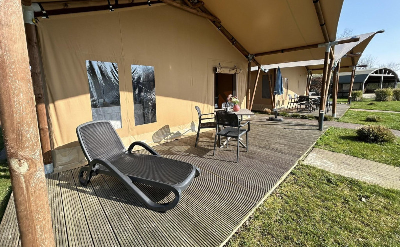 Luxe safaritent met veranda, ligstoel en tuinmeubilair bij Vakantiepark 't Rheezerwold in Nederland.