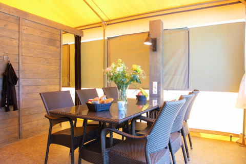 Coin repas sous tente safari de luxe avec chaises en osier et fleurs au Holiday Park 't Rheezerwold, Pays-Bas.