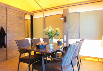 Dining area inside a luxury safari tent with wicker chairs and a flower vase at Holiday Park 't Rheezerwold.