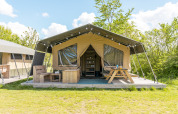 Tienda safari en Camping De Betteld, Países Bajos, con terraza de madera, banco y mesa de picnic al aire libre.